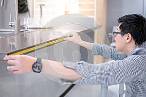 Asian man using tape measure on kitchen counter