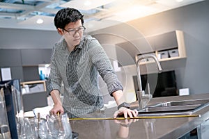 Asian man using tape measure on kitchen counter