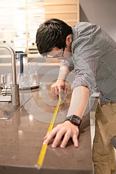 Asian man using tape measure on kitchen counter