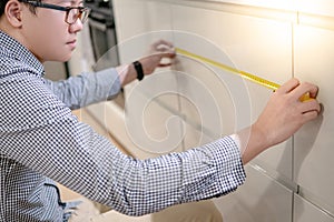 Asian man using tape measure on kitchen counter