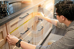 Asian man using tape measure on kitchen counter