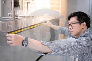 Asian man using tape measure on kitchen counter