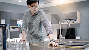 Asian man using tape measure on kitchen counter