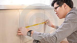 Asian man using tape measure on kitchen counter