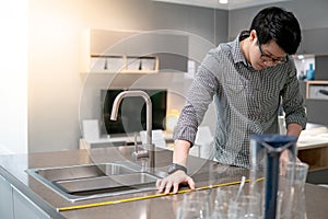 Asian man using tape measure on kitchen counter