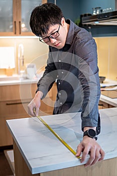 Asian man using tape measure on kitchen counter