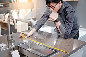 Asian man using tape measure on kitchen counter