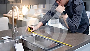 Asian man using tape measure on kitchen counter