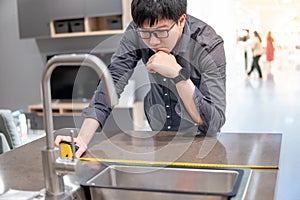 Asian man using tape measure on kitchen counter