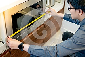 Asian man using tape measure on microwave