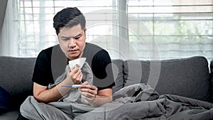 Asian man using tissue to cough, sneezing and using thermometer to checking body temperature when feeling sick