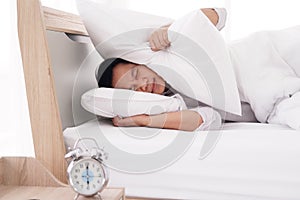 Asian man wake up and alarm clock sounds so loud and noisy. He is  lazy to go to work and sleep on the bed