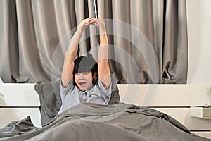 Asian man waking up in bed and stretching his arms.