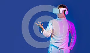 Asian man wear virtual reality vr goggles headset watching touching playing on blue color background. Metaverse concept