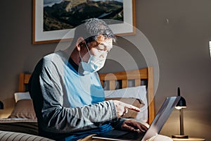 Asian man weared medical mask. Sitting and using laptop in bedroom