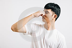 Asian man wearing an anxious expression while pinching his nose due to a strong