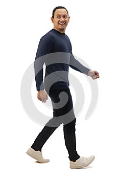 Asian man wearing casual dark blue shirt black denim and white shoes, walking forward and loooking back, side view, happy
