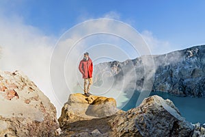 An Asian man wearing a gas mask for safety on Kawah Ijen volcano with turquoise sulfur water lake at sunrise on travel trip and
