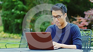 Asian man wearing glasses works with a laptop.