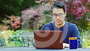 Asian man wearing glasses works with a laptop. Sitting on the summer terrace in the gardens or cafes.