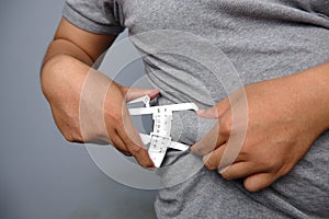 asian man wearing grey shirt checking his fat belly with calipers