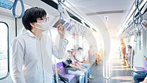 Asian man wearing mask holding handrail on skytrain photo