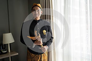 Asian man wearing traditional clothes of indonesian beskap with holding traditional heritage keris