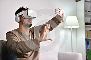 Asian man wearing VR goggles while playing video games with hands reaching out to touch something in virtual world