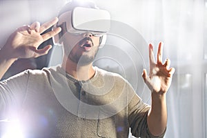 Asian man wearing VR goggles while playing video games with hands reaching out to touch something in virtual world