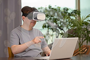 Asian man wearing VR headset and using laptop while sitting at his desk