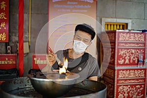 Asian man wearing a white mask lights incense on an oil burner in a shrine. photo