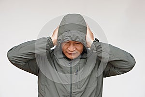 Asian man wears hoodie, uses his hands to cover ears. Concept, don\'t want to listen or hear anything.