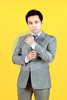 Asian man well dressed in a gray suit and white shirt, standing against a yellow background. A businessman Crossing his arms with