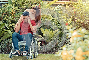 Asian Man in a wheelchair and Unhappy and painful. A woman standing behind the wheelchair and is encouraging her husband, whose fe