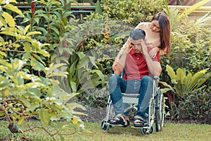 Asian Man in a wheelchair and Unhappy and painful. A woman standing behind the wheelchair and is encouraging her husband, whose fe