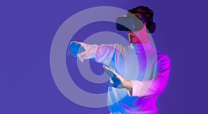 Asian man in white long sleeve t-shirt wear vr goggles headset watching playing touching game online purple background. Metaverse