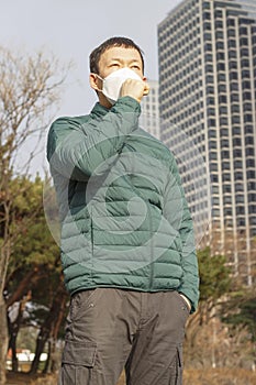 Asian man in white mask coughs and covers his face with his hand on the background of the city
