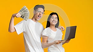 Asian man and woman earning online, holding laptop and dollars