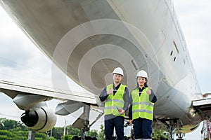 Asian man and woman engineer maintenance airplane thumb up and holding wrench in front airplane from repairs, fixes, modernization