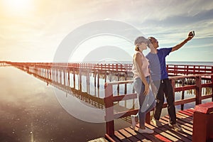 asian man and woman taking a photo on red wood bridge against sun rising sky