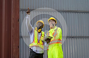 Asian man worker holding walkie-talkie and African engineer holding digital tablet working together at cargo shipping for