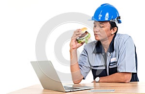 Asian man worker smiling and holding a hamburger in the living room While working from home, hem very happy and enjoy to eat fast