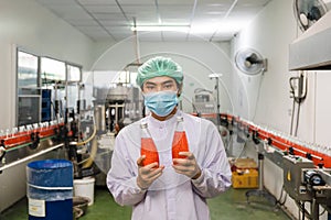 Asian man worker in sterile uniform showing product of bottled red juice in production line at beverage processing factory