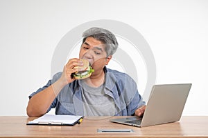 Asian man working and eating a burger on the office desk. Concept of a busy businessman cannot work-left balance and not taking