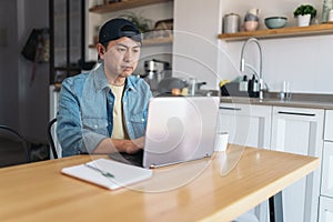 Asian man working with a laptop from the kitchen