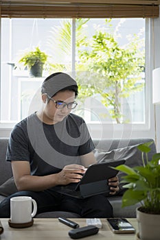 Asian man working online with computer tablet while sitting on couch.