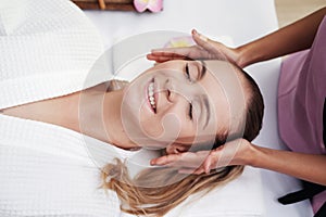 Asian Massage therapist woman is making traditional head and facial treatment massage to Caucasian female is relaxing and smilng