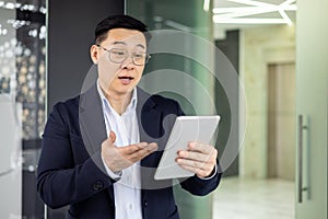 Asian mature man in business attire using a tablet in modern office environment