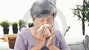 Asian Mature woman with allergy sneezing and blowing her nose in a tissue, 4K slow motion.