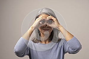 Asian mature woman does ok gesture like binoculars.